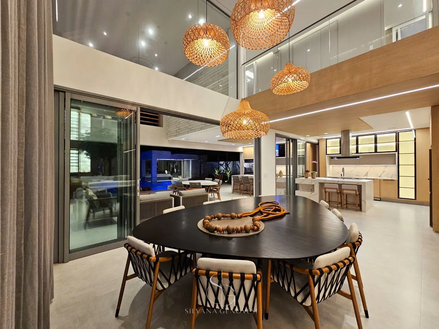 Sala de jantar com mesa orgânica escura, cadeiras de madeira trançada e luminárias de fibra natural