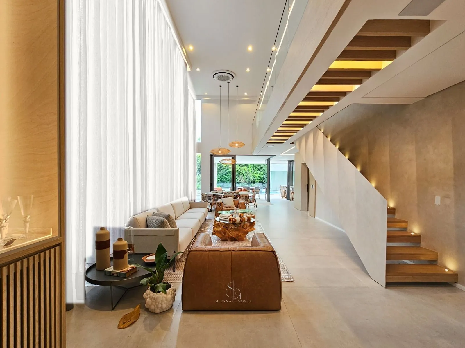 Living com pé-direito duplo, cortinas de linho, escada de madeira e abertura para o jardim